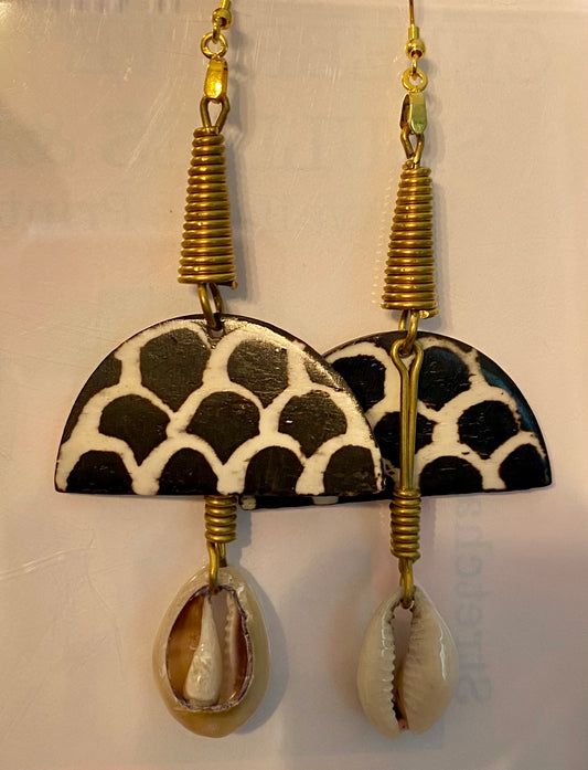 Pair of earrings with black and white patterned half-circle design and cowrie shell accents on a light background.