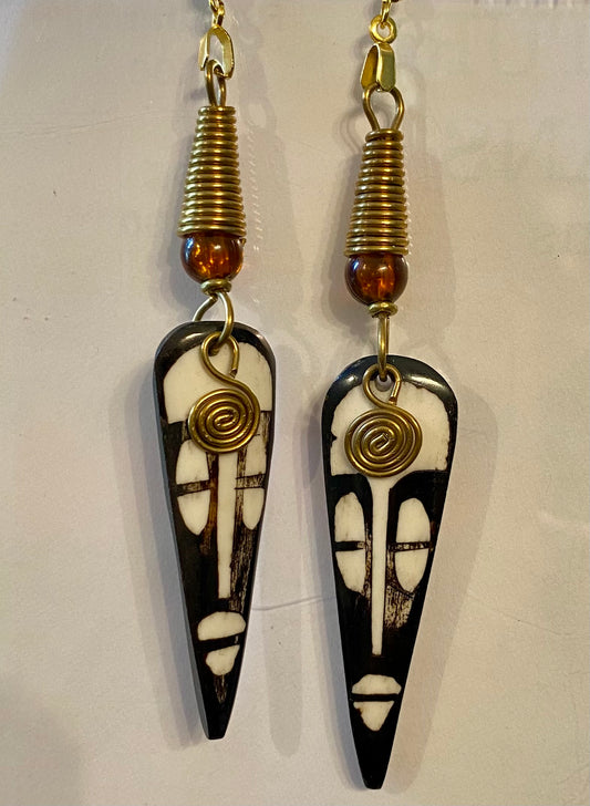 Pair of black and white mask earrings with gold and amber accents on a light background